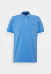 Světle modrá polo košile z jemné bavlny, s klasickým límcem, třemi knoflíky a diskrétně vyšitou logem na hrudi.