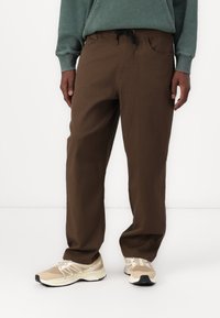 Pantalones marrones de corte relajado con cintura elástica y cordón ajustable. Incluyen además dos bolsillos laterales, confeccionados en una tela duradera.