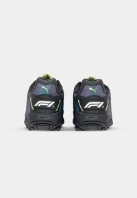 Puma F1 bateliai su juodu, žaliu ir mėlynu sintetiniu paviršiumi; tekstūruota tinklinė apykaklė; balta logotipas; užpakalinis amortizacijos dizainas; guminis padas.