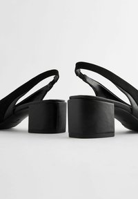 Crne slingback platform cipele s teksturiranim nubuk gornjim dijelom, zaobljenim vrhom i debelim, čvrstim blok petama. Čist, minimalistički dizajn.