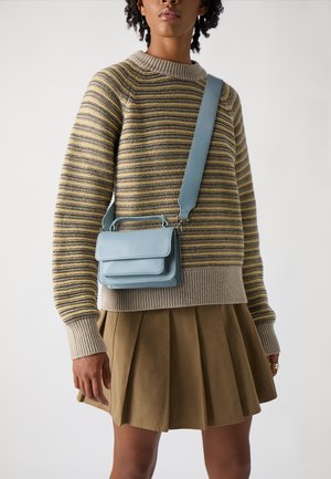 Borsa a tracolla in pelle blu chiaro con design strutturato, chiusura a pattina anteriore e manico corto, indossata sopra un maglione a righe e una gonna plissettata.