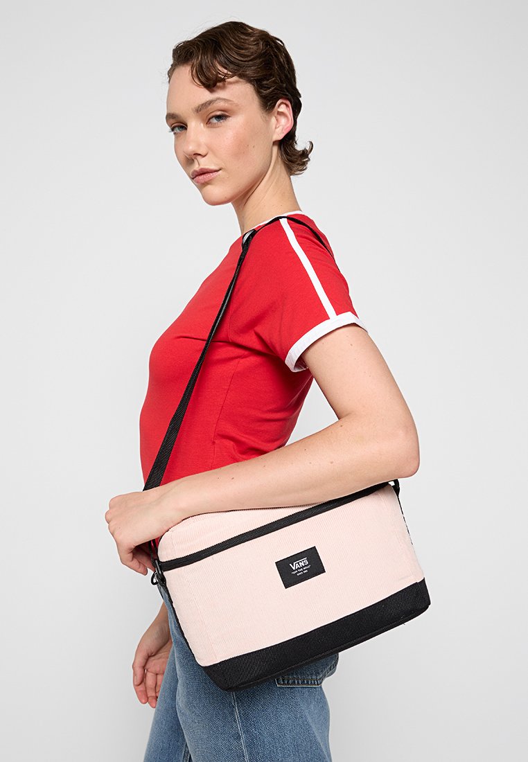 Bolso cruzado con un cuerpo texturizado color crema y base negra, con cierre de cremallera y parche de logo. Correa ajustable para mayor comodidad al llevarlo.