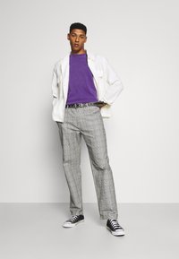 Purple crew-neck sweater, white button-up jacket, gray plaid trousers, and black sneakers. Simple design and casual fit, with a belt accent.