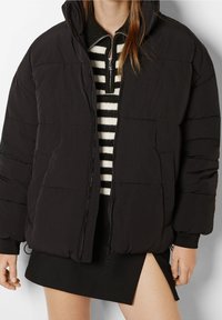 Czarna kurtka puchowa z zapięciem na zamek, z wysokim kołnierzem i ściągaczami na rękawach. Projekt obejmuje pikowaną fakturę z poziomymi szwami.