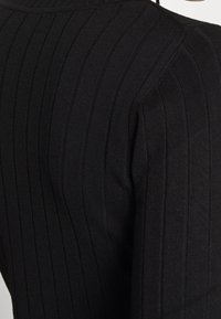 Schwarz geripptes Strickoberteil mit hohem Kragen, das vertikale Streifen und eine taillierte Passform präsentiert und Textur sowie Form betont.