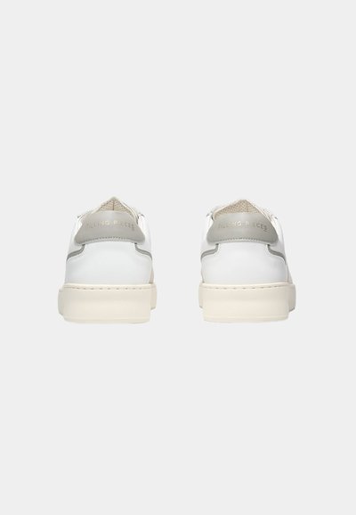 Par hvite lave sneakers vist bakfra med lysegrå hælfliker og tykke offwhite såler mot en ensfarget bakgrunn.