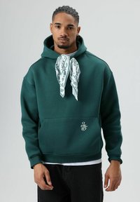 Groene katoenen hoodie met een voorvak, geribbelde manchetten en een witte bandana met paisley-patroon gestrikt rond de nek. Logo aan de voorkant.