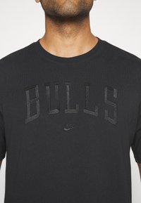 Černé bavlněné tričko s texturovaným vyšitým logem "BULLS" a malým logem Nike pod nápisem.
