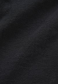 Tissu noir avec une texture subtile en chevrons et de douces plis créant des variations de lumière et d'ombre.