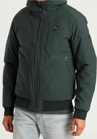 Mörkgrön isolerad jacka med huva, med en framsida som har dragkedja, två sidofickor och en logotyp-patch på bröstet. Ribbad mudd och midja.