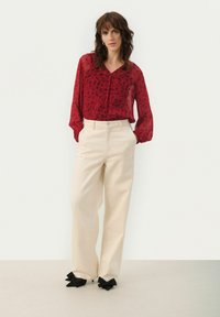 Blusa transparente de estampado floral rojo con escote en V, combinada con pantalones de pierna ancha beige de cintura alta y zapatos negros con lazo.