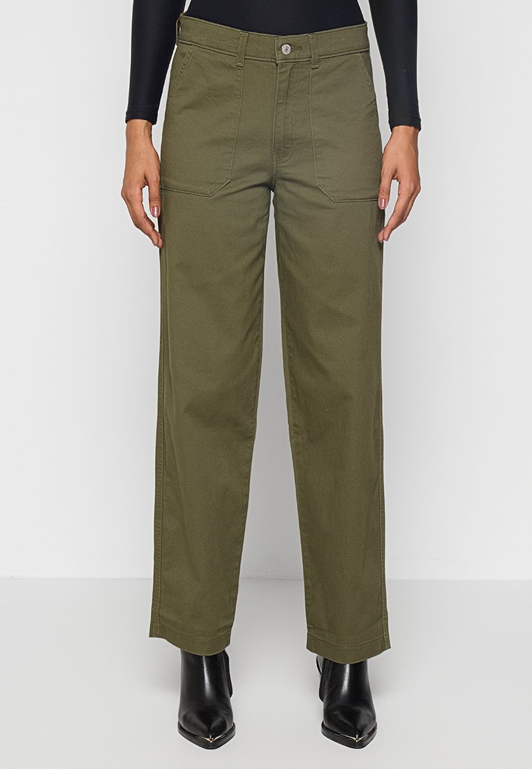 Pantalons larges vert olive en tissu coton, dotés de poches avant et d'une fermeture à boutons, associés à des bottes noires à bout pointu.