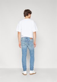Vit bomulls t-shirt med kort ärm, parat med ljusblå slim-fit denimjeans, med en läderlapp på baksidan av midjebandet.