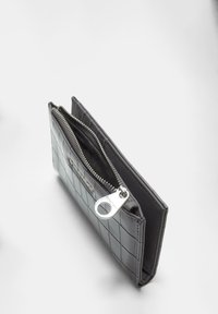 Schwarze Reißverschlussbörse mit einem gesteppten Muster, das eine glänzende Oberfläche und einen silberfarbenen Reißverschluss-Zipper aufweist, der die Innenfächer präsentiert.