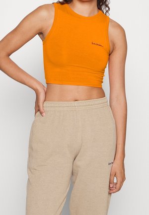 Orange cropped top i blødt stof med rund halsudskæring og lille sort tekst. Kombineret med lyse beige sweatpants.