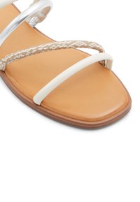 Płaskie sandały z brązową wkładką, z białymi i plecionymi beżowymi paskami oraz metalicznym srebrnym akcentem. Gładka tekstura z kwadratowym czubkiem.