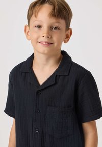 Mørkeblå kortærmet skjorte i tekstureret stof med krave, tre knapper og brystlomme med præget detalje.