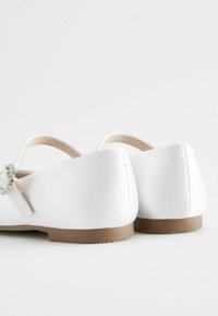 Ballerines blanches à finition satinée, avec un bout rond, un petit talon et une sangle décorative agrémentée d'une boucle en ton argent.