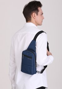 Borsa a tracolla blu realizzata in tessuto testurizzato, dotata di un compartimento principale con cerniera, una tasca frontale e una tracolla regolabile.