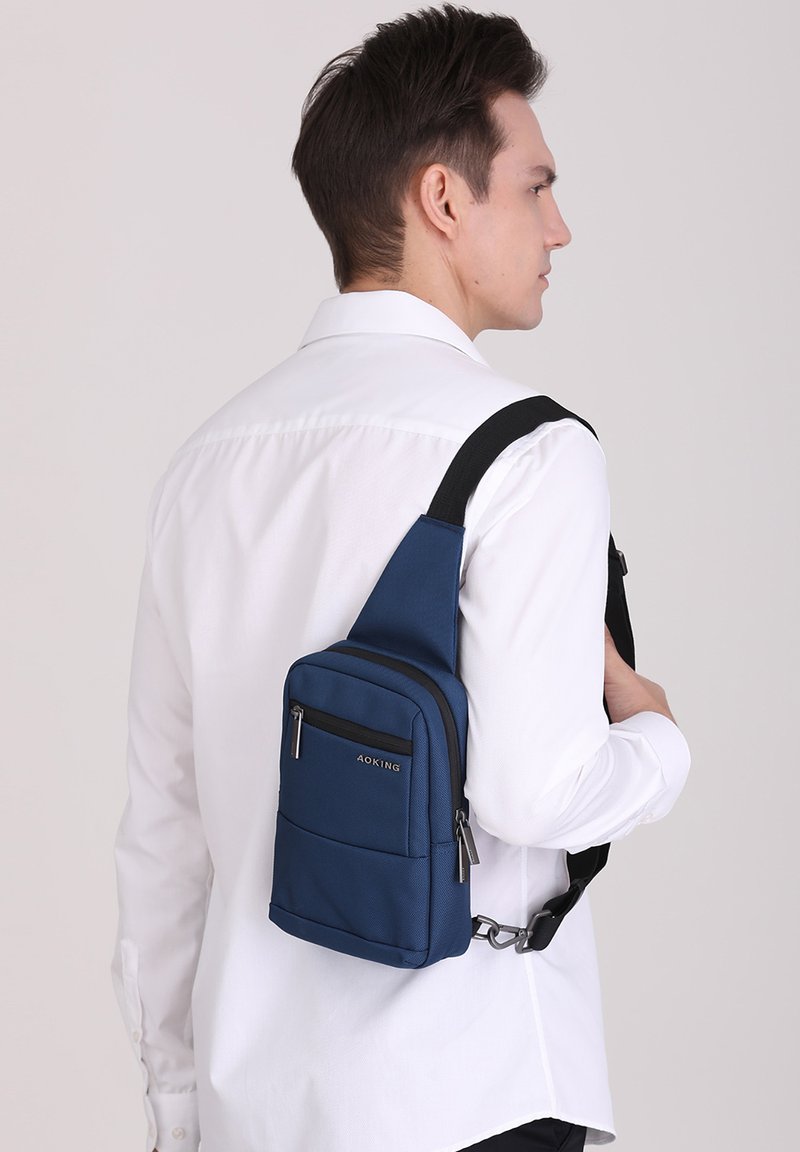 Borsa a tracolla blu realizzata in tessuto testurizzato, dotata di un compartimento principale con cerniera, una tasca frontale e una tracolla regolabile.