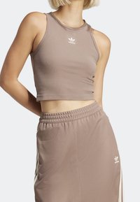 Brązowy prążkowany crop top bez rękawów z małym białym logo adidas na środku klatki piersiowej, w zestawie z pasującymi spodniami na sznurek.