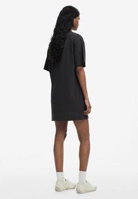 Ylihuokattu tumma harmaa t-paitamekko, jossa on lyhyet hihat, sivurei'itykset ja pehmeä puuvillakangas. Mekko on yhdistetty valkoisiin nilkkasukkia ja vaaleisiin lenkkareihin.