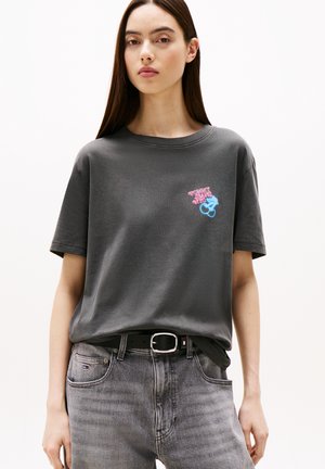 Camiseta de algodón gris con corte holgado y mangas cortas, que presenta coloridos acentos gráficos y "TOMMY JEANS" en el pecho.
