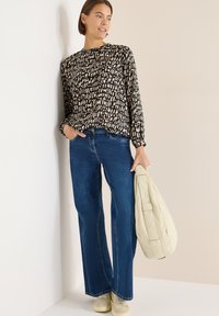 Musta-beige kuvioitu pitkähiha-paita, siniset leveälahkeiset farkut ja beiget lenkkarit. Pitelee vaaleanbeigeä tikattua laukkua.