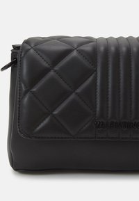 Black quilted leather bag featuring a smooth finish, diagonal ribbed design, and embossed brand logo on the front. Zipper closure at the top.