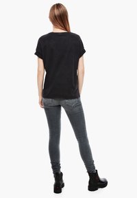 Camiseta negra de gran tamaño con mangas enrolladas, combinada con jeans ajustados grises y botas negras hasta el tobillo. El conjunto presenta un diseño casual y relajado.