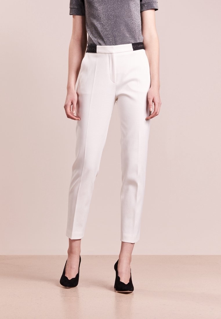 Pantalons blancs sur mesure avec une texture lisse, présentant une ceinture noire en accent. Le design est ajusté avec des lignes épurées et une longueur raccourcie.