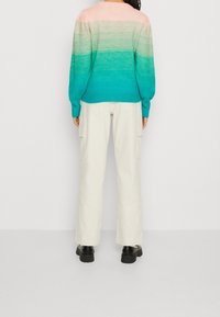 Pletený svetr s odstínem pastelové růžové přecházející do tyrkysové s žebrovanou texturou. Doplněno krémovými kalhotami s širokými nohavicemi a černou obuví.