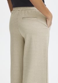 Pantalons beiges texturés avec un petit motif à carreaux. Comprend une taille élastique et une poche arrière avec un subtil détail de couture.