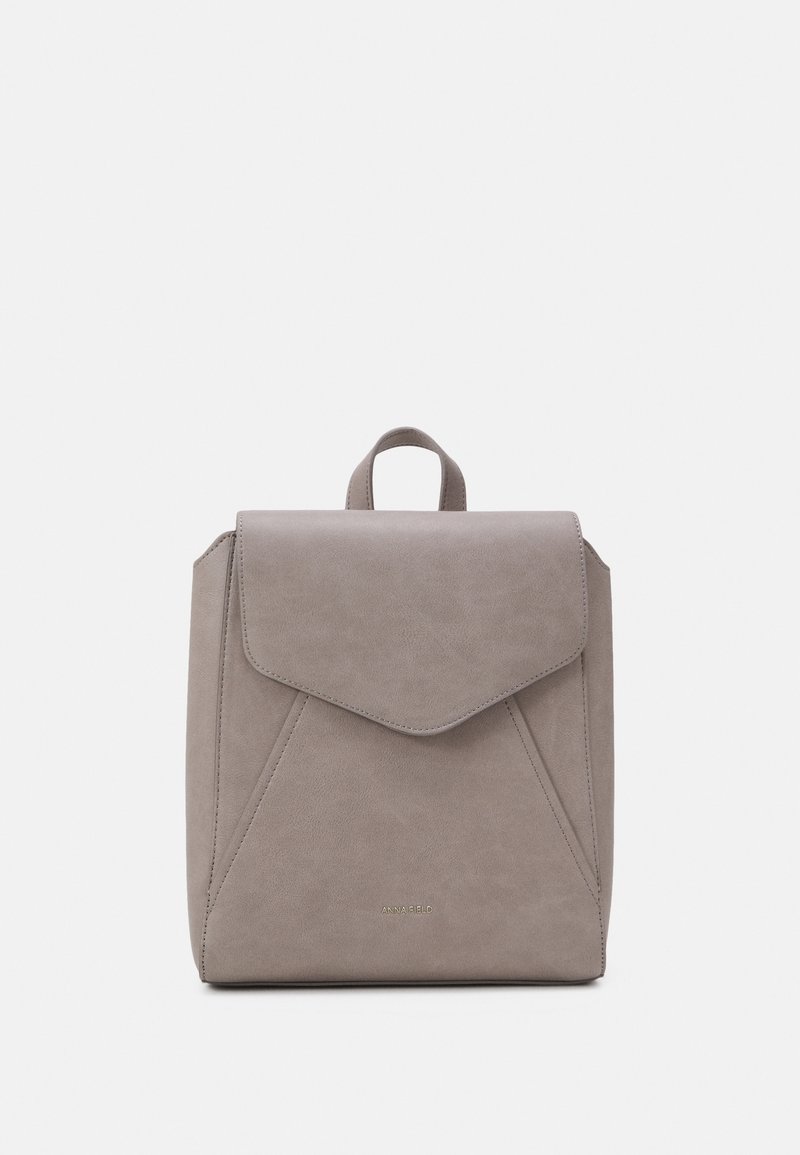 Mochila pequeña de ante color topo con una solapa frontal, un asa en la parte superior y un sutil logo de "Anna Field" en la parte central inferior.