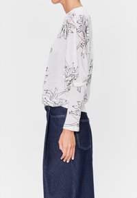 Långärmad topp i ljusgrått med svart blommönster. Mjuk tyg, avslappnad passform och rundad halsringning. Matchad med en mörk denimkjol.