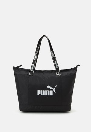Czarna torba typu tote marki Puma z białym logo z przodu, dwoma czarnymi paskami na ramię z powtarzającym się białym logo Puma oraz zamkiem błyskawicznym na górze.