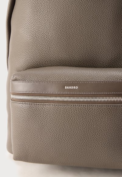 Τσάντα πλάτης από δέρμα ταμπά με υφή στο μπροστινό μέρος, ασημένιο φερμουάρ και λογότυπο SANDRO στο περίγραμμα της τσέπης.