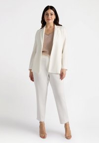 Vit blazerset och byxor i en mjuk tyg, parat med en beige ribbad topp. Anmärkningsvärda detaljer inkluderar strukturerade blazerlappar och byxor i ankellängd.