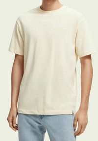 T-shirt a maniche corte in cotone color crema con collo rotondo e piccolo logo verde sul petto. Vestibilità rilassata con orlo dritto.