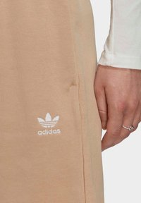 Beżowa bawełniana bluza z kapturem z przednią kieszenią, prążkowaną fakturą i białym haftowanym logo z trzema paskami, noszona z koszulą z długim rękawem.