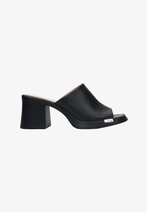 Mules à talon bloc noirs avec une surface lisse et brillante, un design à bout ouvert et un accent logo métallique subtil sur le côté.