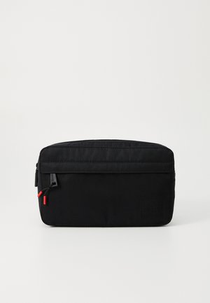 Schwarze Stofftasche mit glatter Textur, mit einem Reißverschluss und roten Ziehbanden. Verfügt über eine Vordertasche und eine geprägte Markenkennzeichnung an der Seite.