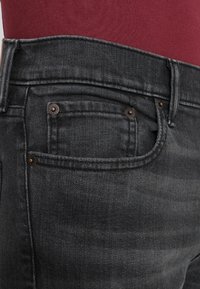 Svarta denimjeans med en standarddesign med fem fickor, kopparnipplar och en något texturerad yta. Midjan stängs med en knapp.