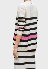 Pruhovaný svetr v barvách krémové, černé a růžové. Má dlouhé rukávy, volný střih a horizontální pruhy. Měkká látka s žebrovanými manžetami.