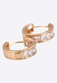 Boucles d'oreilles en or avec un incrustation de cristal transparent taillé en triangle, mettant en valeur une surface métallique lisse et un système de fermoir sécurisé.