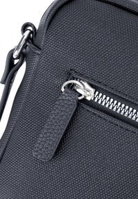 Schwarze, strukturierte Stoff-Umhängetasche mit einem silbernen Reißverschluss, flachem Leder-Zip-Zipper und metallischen Hardware-Akzenten. Kompakte und strukturierte Form.