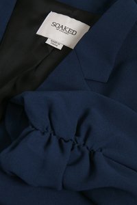 Jakna mornarsko plave boje s detaljem skupljene tkanine i crnim podstavom, prikazuje oznaku "SOAKED in Luxury" i oznaku "Made in China".