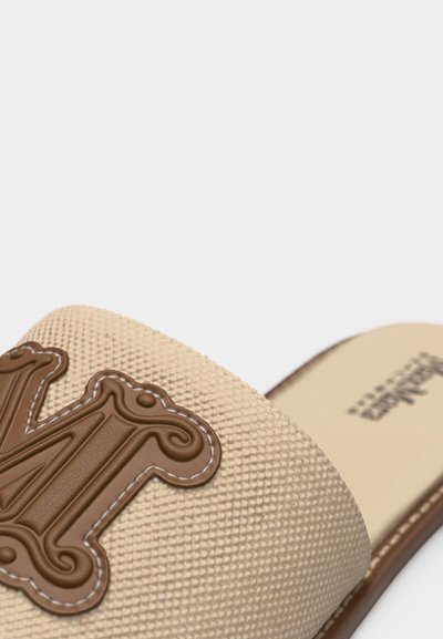 Μπεζ υφασμάτινο σανδάλι με καφέ διακοσμητικό κέντημα στο λουρί και εμφανές όνομα μάρκας στη σόλα.