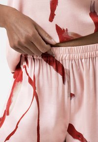 Lichtroze stof met rode abstracte patronen, voorzien van een elastische tailleband en een comfortabele pasvorm, gedeeltelijk weergegeven met een hand die de bovenkant aanpast.