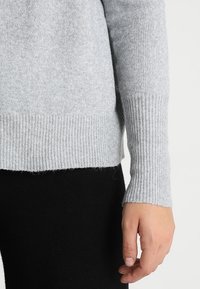 Lichtgrijze gebreide trui met geribde manchetten, met een zachte textuur en een iets cropped zoom, gecombineerd met donker zwarte broek.